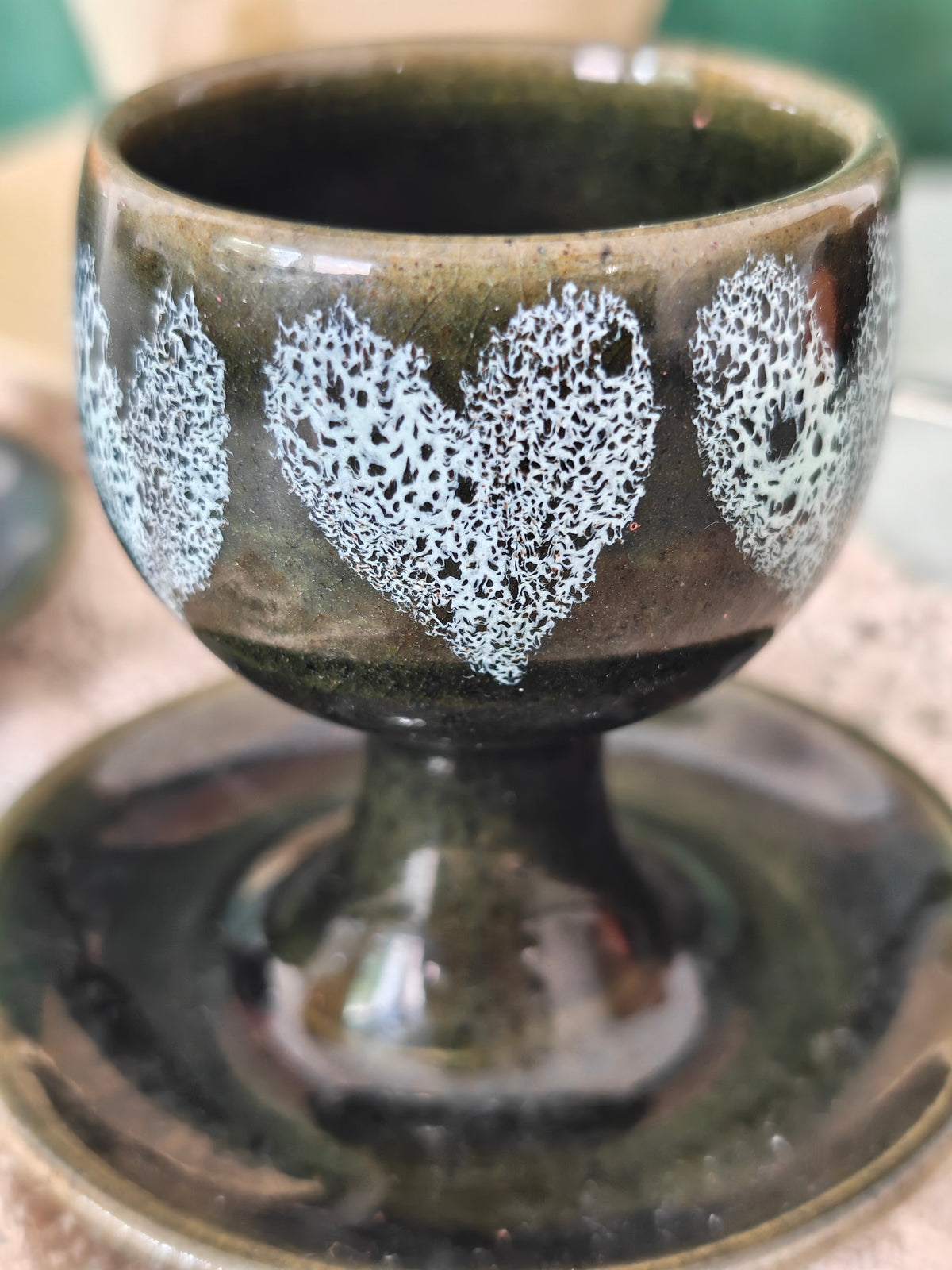 A dark green ceramic egg cups with white heart pattern and attached saucer. 