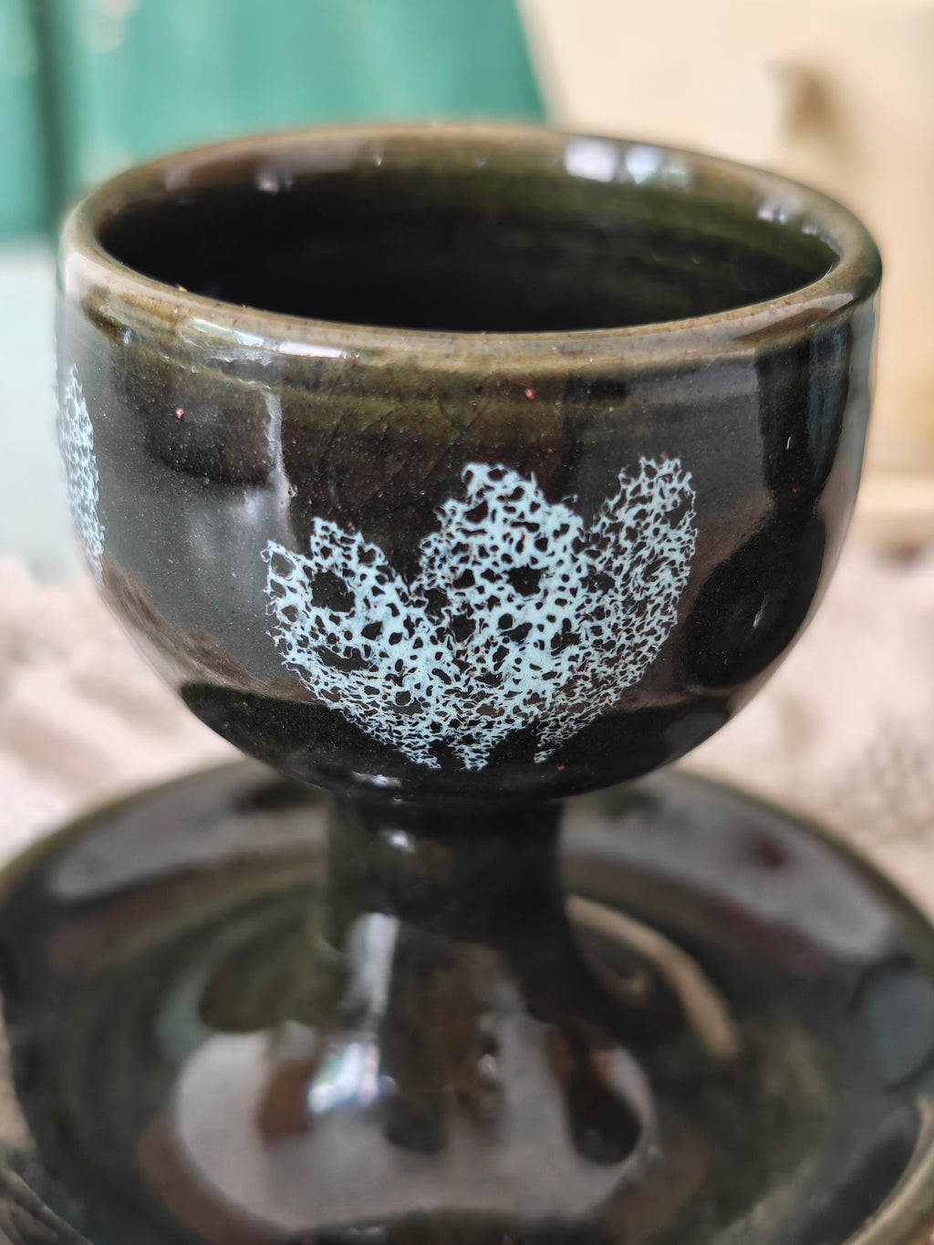 A dark green ceramic egg cup with white floral patterns and attached saucer. 