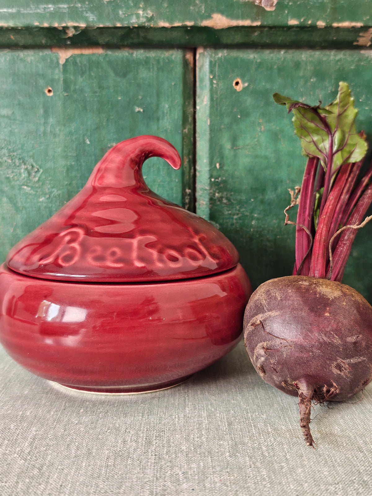 A glossy red ceramic lidded jar with a sculpted lid resembling a beetroot and embossed text.