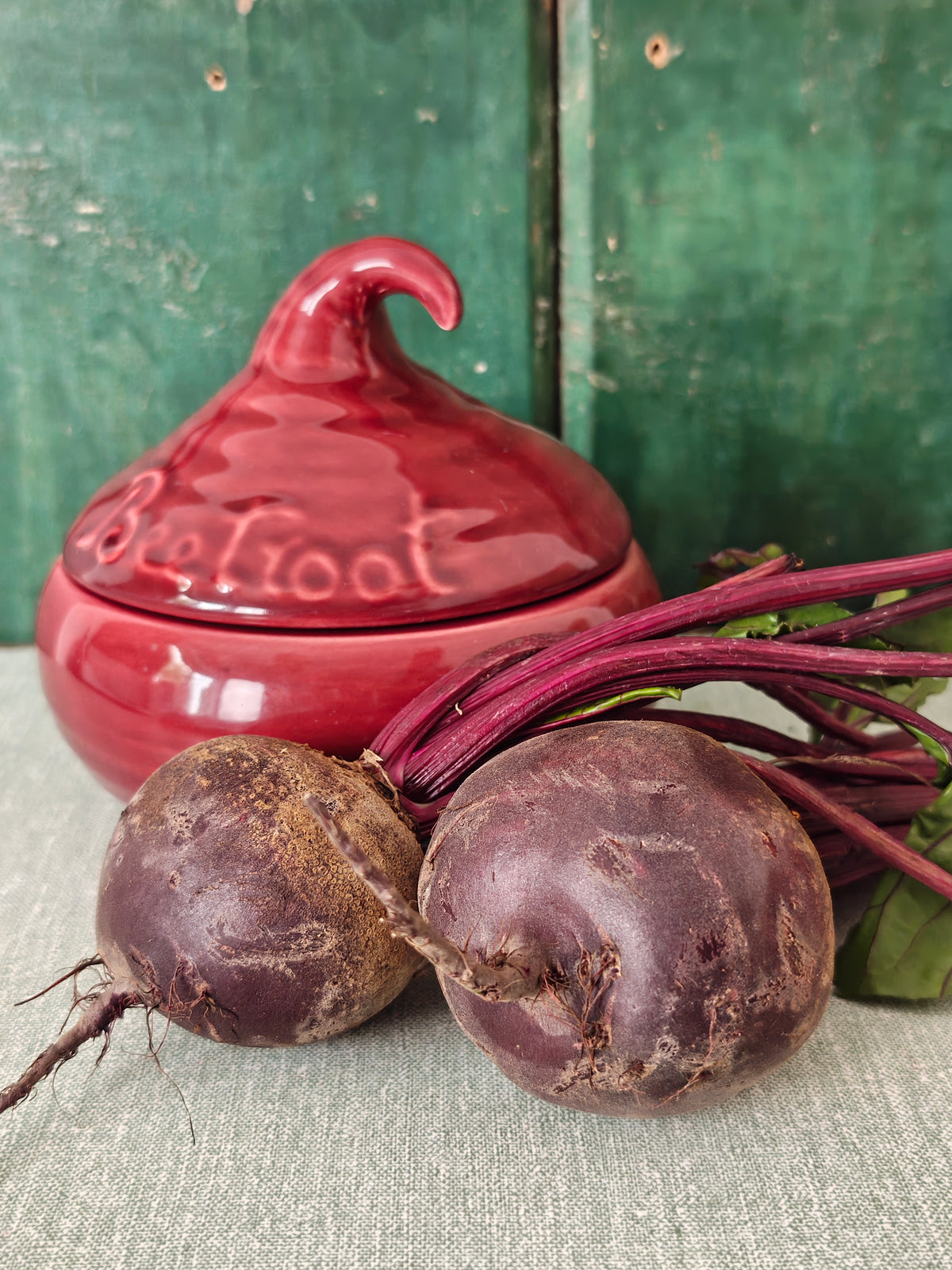 A glossy red ceramic lidded jar with a sculpted lid resembling a beetroot and embossed text.