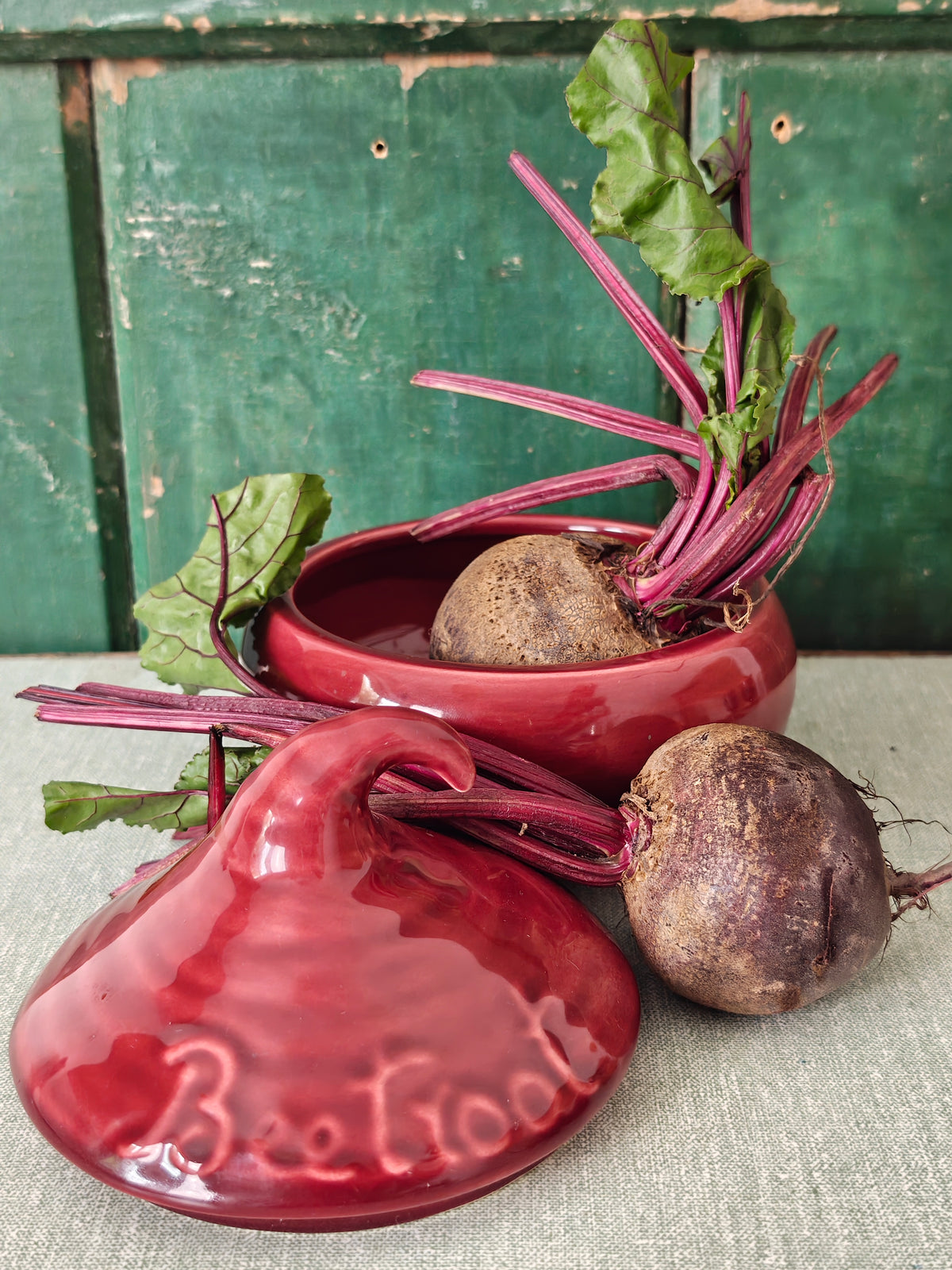 A glossy red ceramic beetroot pot with its lid placed in front.