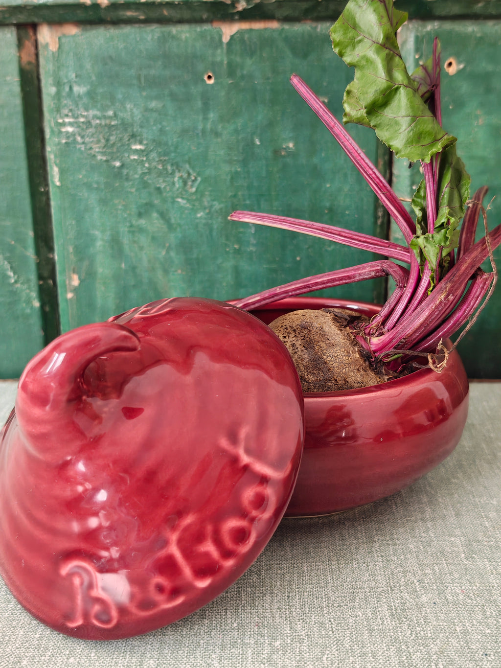 A glossy red ceramic beetroot pot with its lid leaning against it.