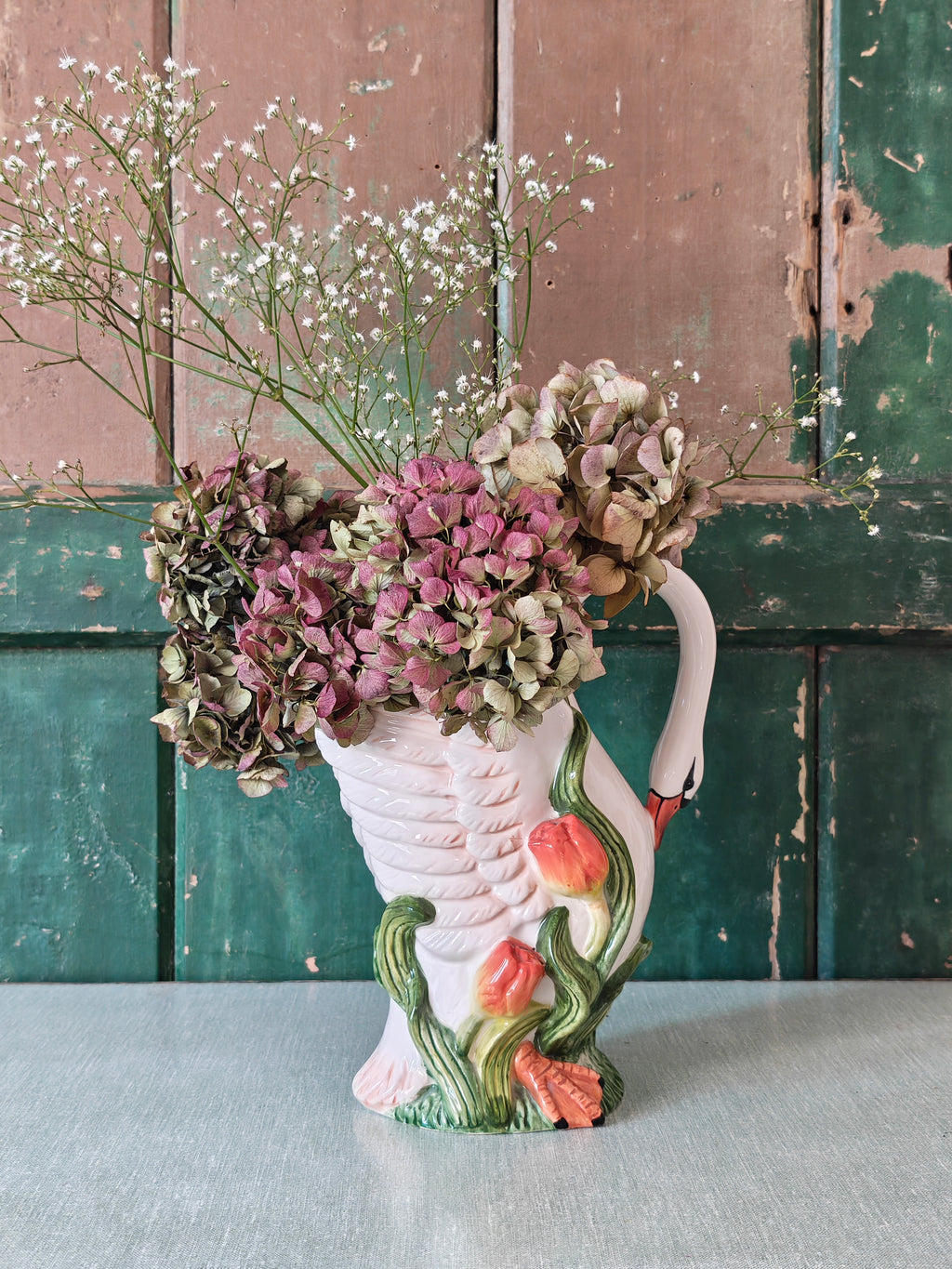 A white ceramic swan-shaped pitcher featuring green leaves and orange tulips near the base.