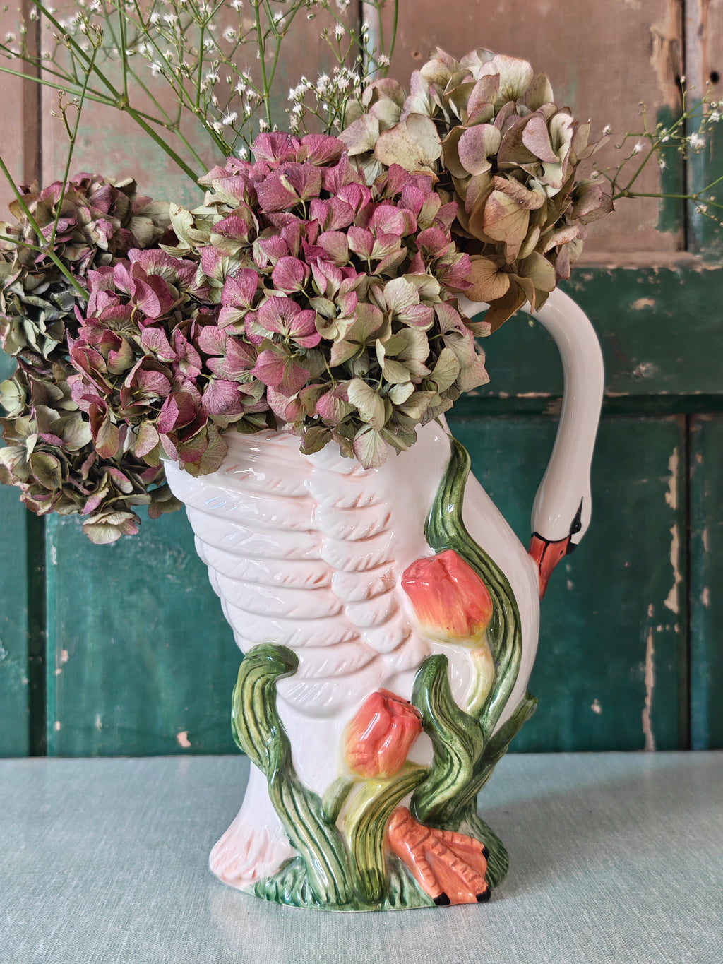 A white ceramic swan-shaped pitcher featuring green leaves and orange tulips near the base.
