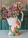 A white ceramic swan-shaped pitcher featuring green leaves and orange tulips near the base.