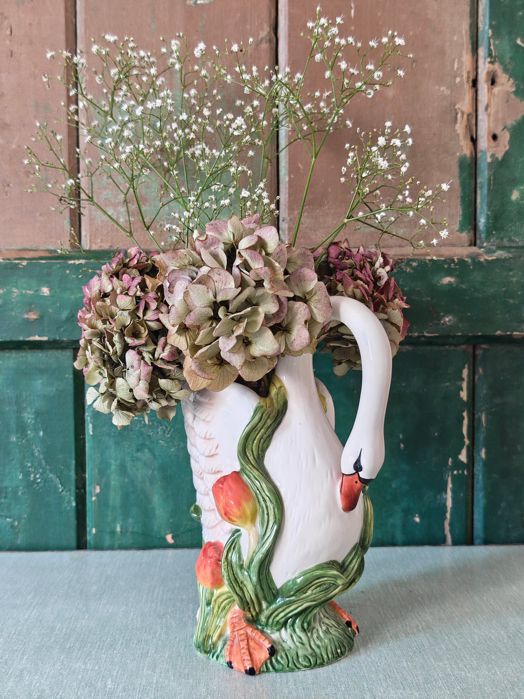 A white ceramic swan-shaped pitcher featuring green leaves and orange tulips near the base.
