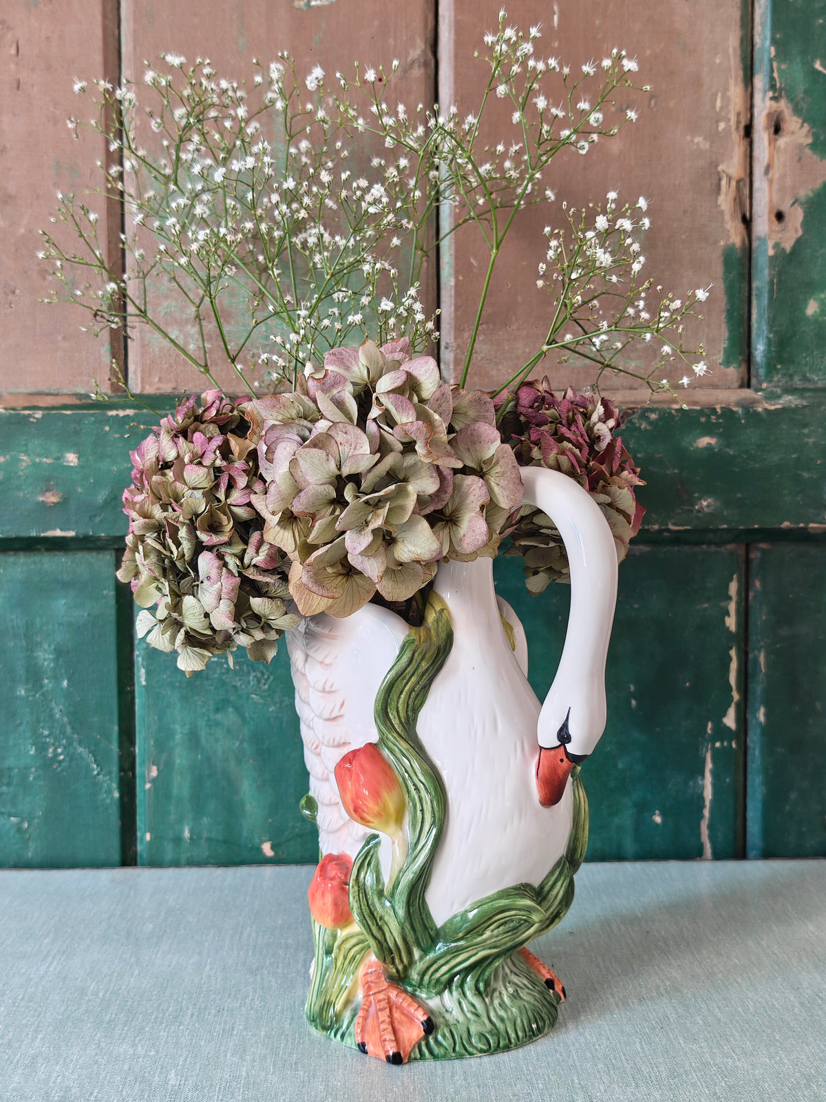 A white ceramic swan-shaped pitcher featuring green leaves and orange tulips near the base.