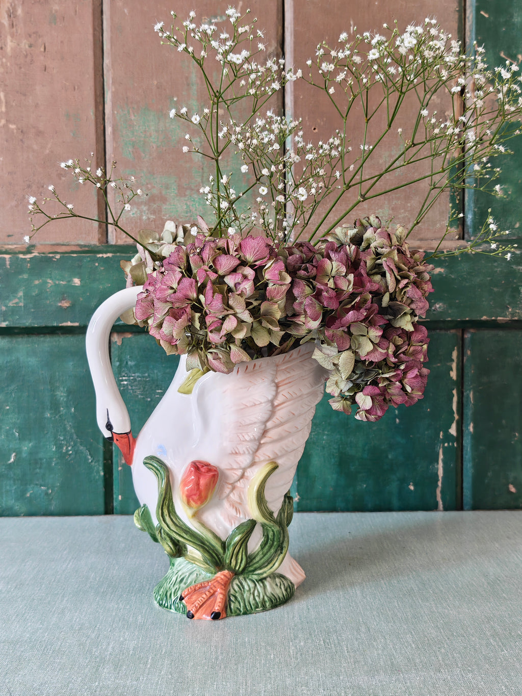 A white ceramic swan-shaped pitcher featuring green leaves and orange tulips near the base.