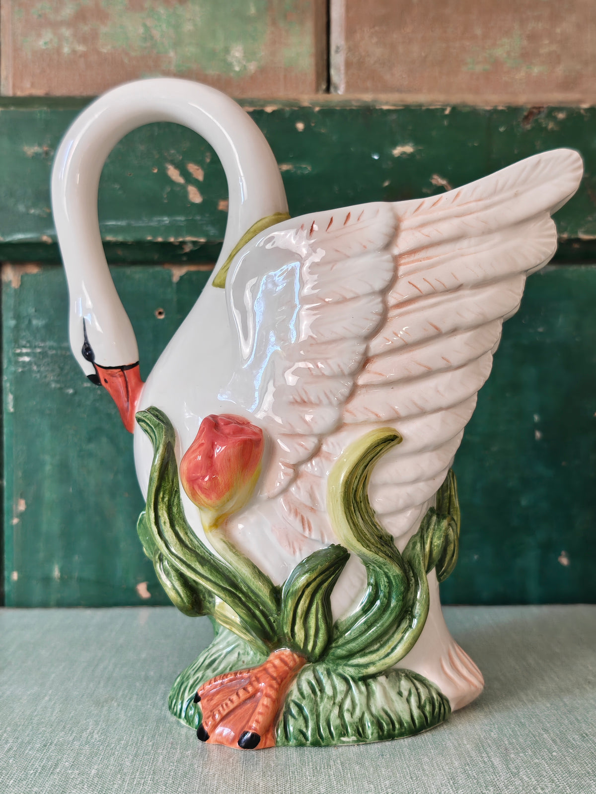 A white ceramic swan-shaped pitcher featuring green leaves and orange tulips near the base.