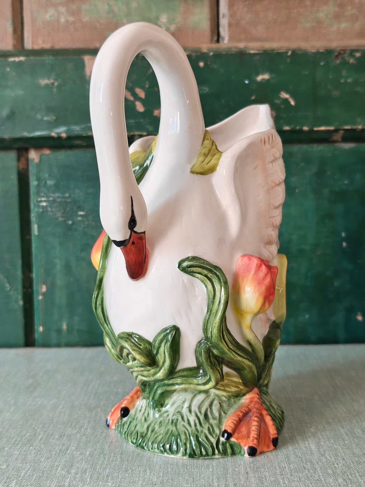 A white ceramic swan-shaped pitcher featuring green leaves and orange tulips near the base.