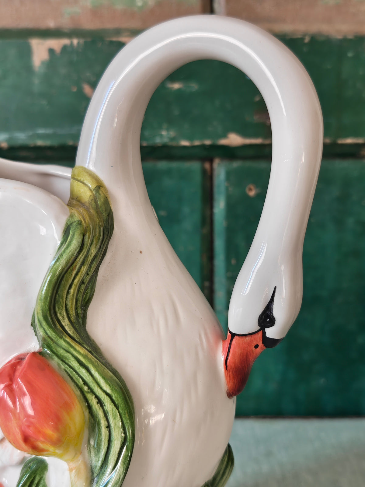 Close-up of  the head and neck of a ceramic swan pitcher with green leaves and a tulip