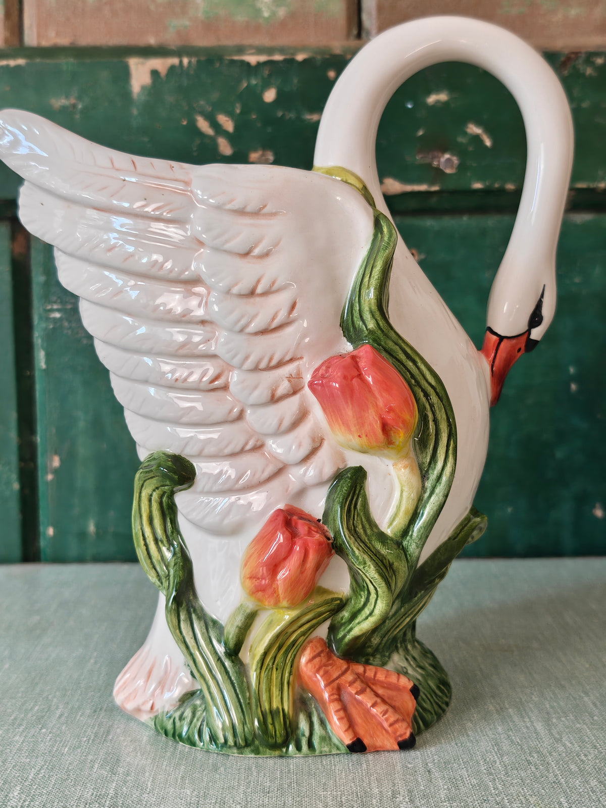 A white ceramic swan-shaped pitcher featuring green leaves and orange tulips near the base.