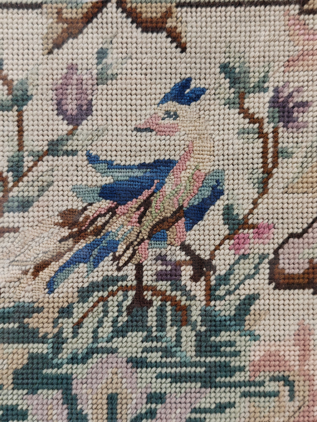 Close-up of a needlepoint canvas featuring a detailed crest design with a bluebird, floral elements, and a beige background.