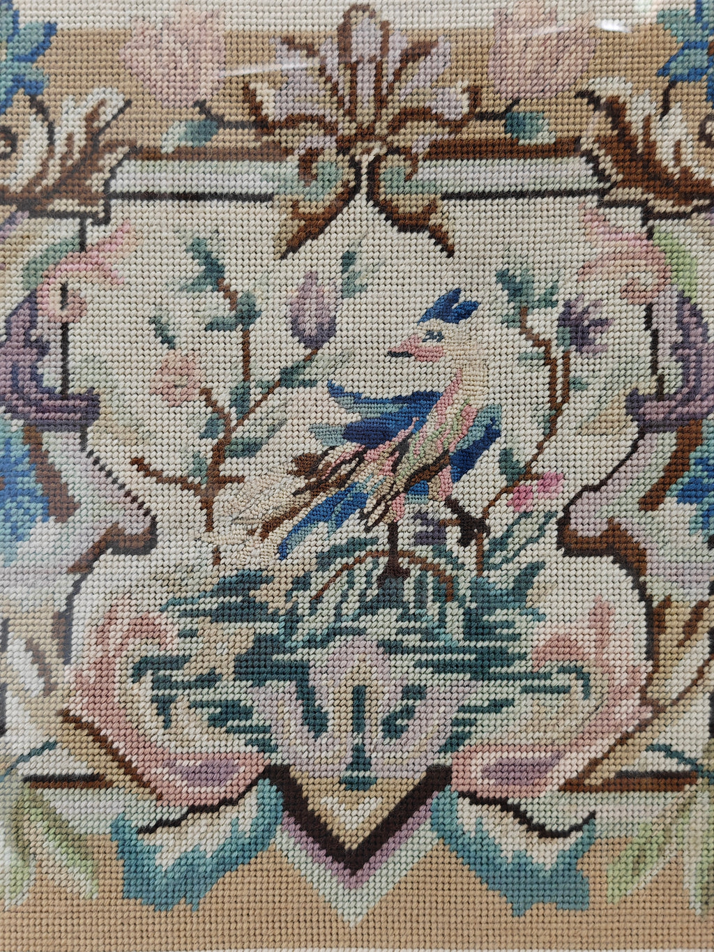 Close-up of a needlepoint canvas featuring a detailed crest design with a bluebird, floral elements, and a beige background.