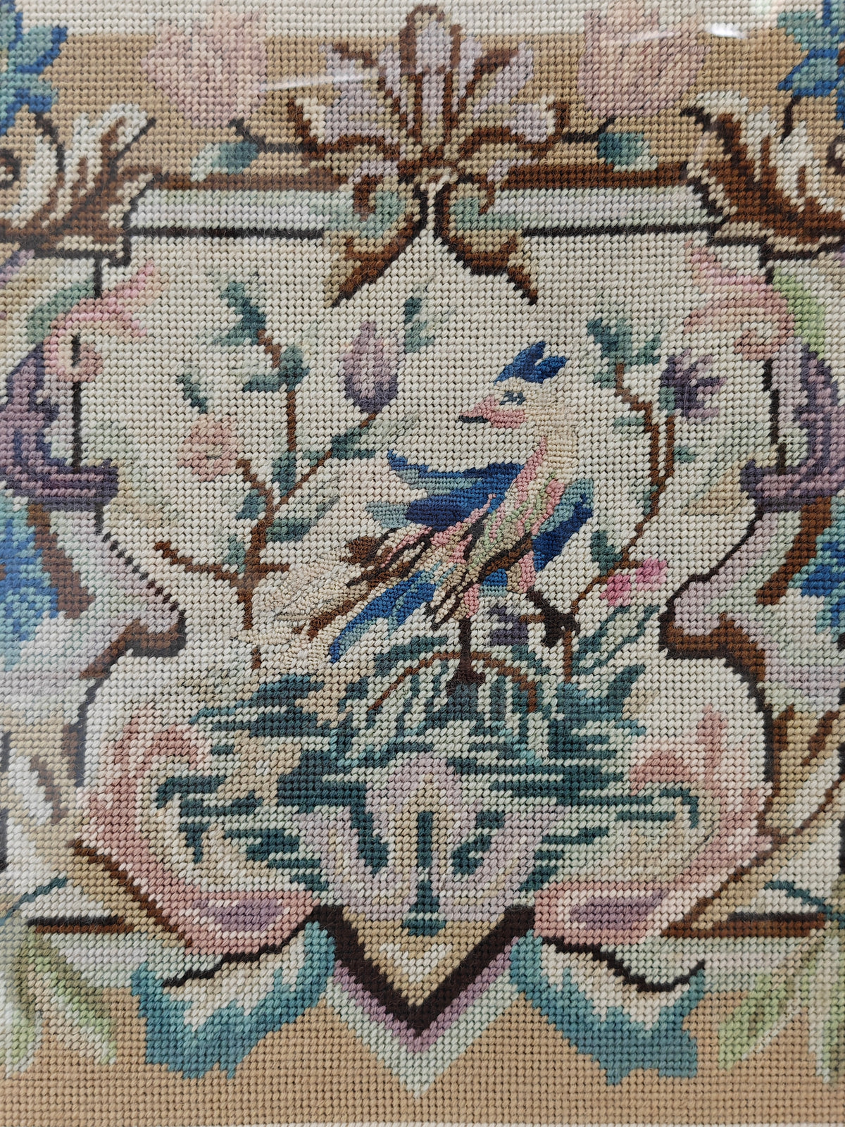 Close-up of a needlepoint canvas featuring a detailed crest design with a bluebird, floral elements, and a beige background.