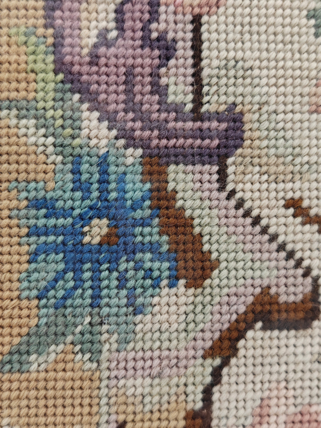 Close-up detail of a needlepoint canvas showing the embroidered floral pattern with pink, green, blue, and brown stitched details.