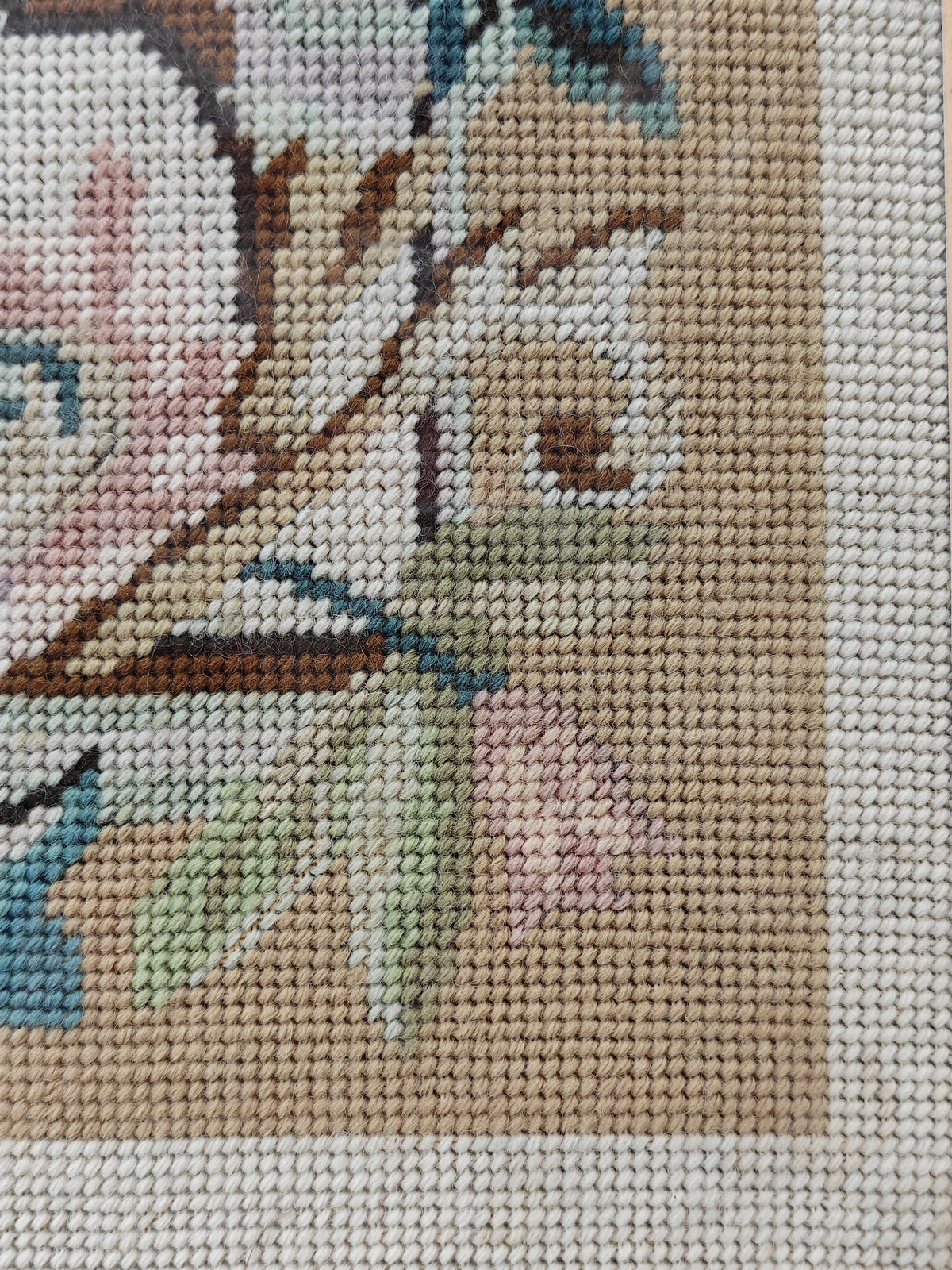 Close-up detail of a needlepoint canvas showing the embroidered floral pattern with pink, green, blue, and brown stitched details.