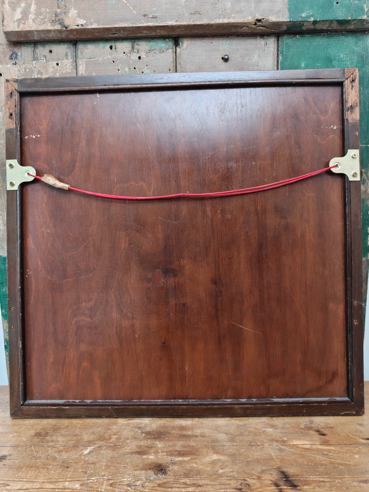 The back of a square framed artwork or panel, showing a dark brown wooden frame.