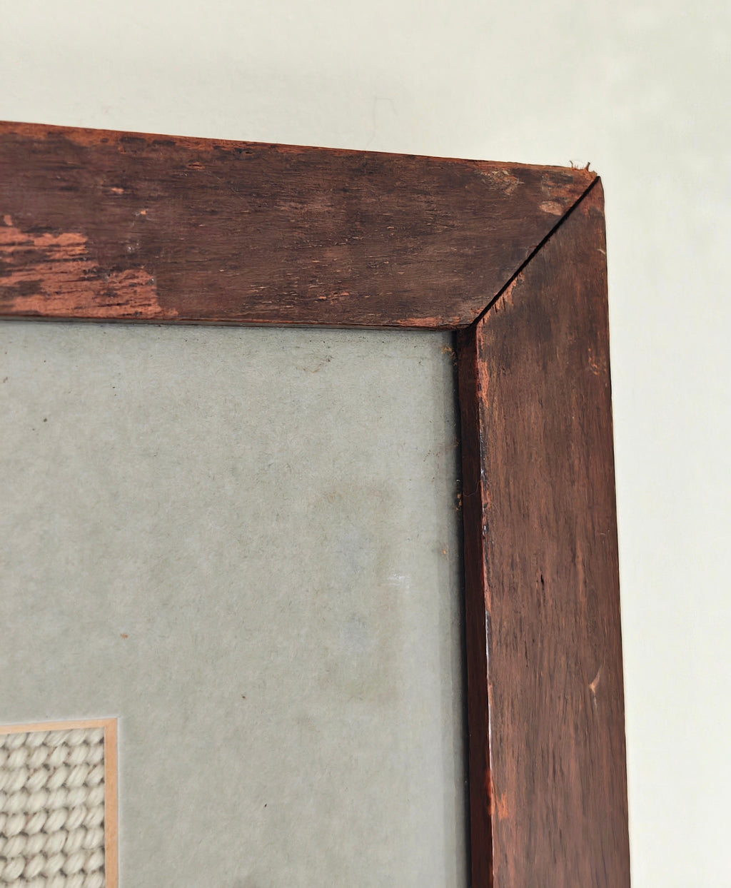 Close-up of a dark brown wooden picture frame corner with distressed, peeling paint showing a warm wood tone underneath
