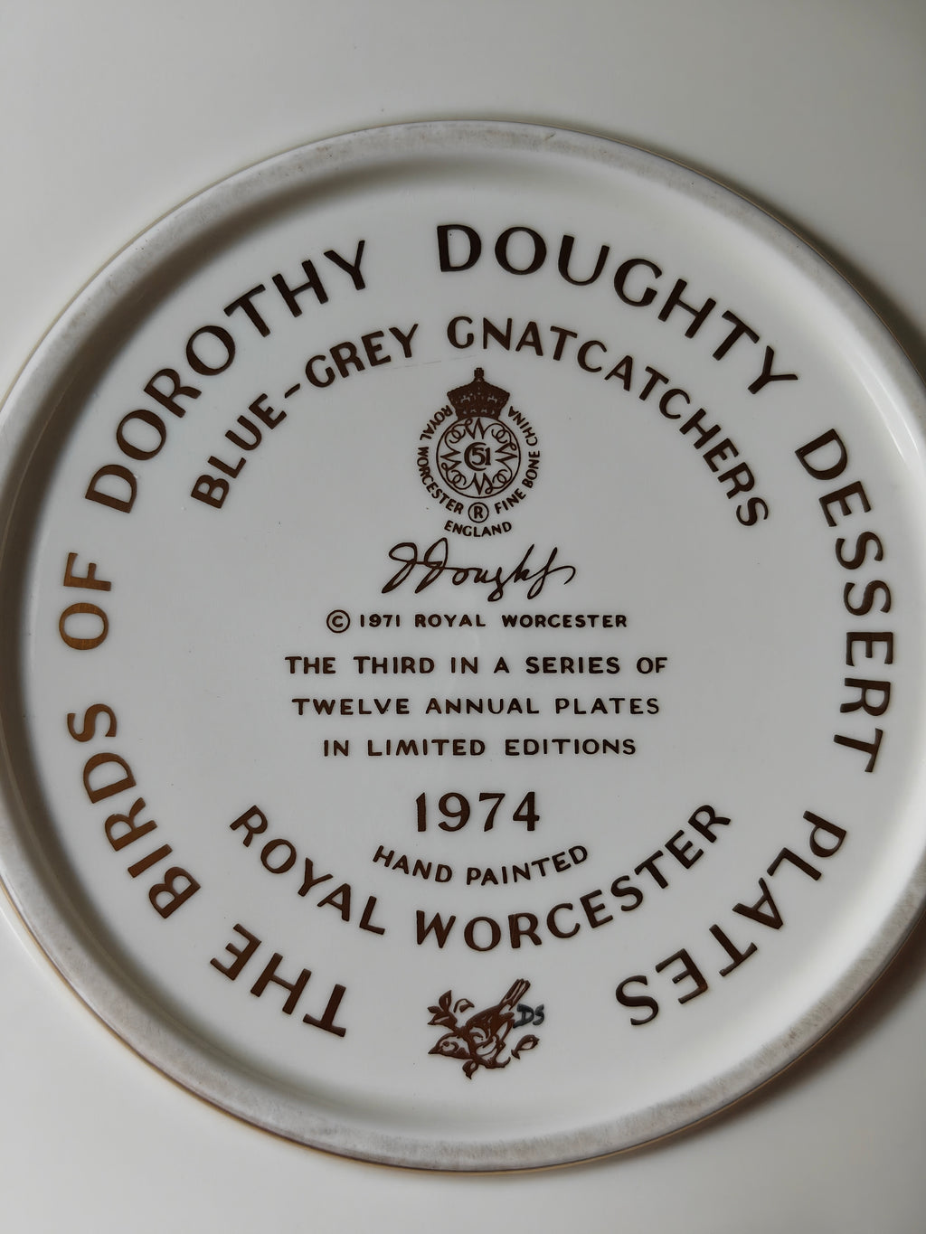 A close-up of the back of a Royal Worcester hand-painted ceramic plate, featuring brown printed text and logo for 'The Birds of Dorothy Doughty Dessert Plates' and 'Blue-Grey Gnatcatchers 1974'.