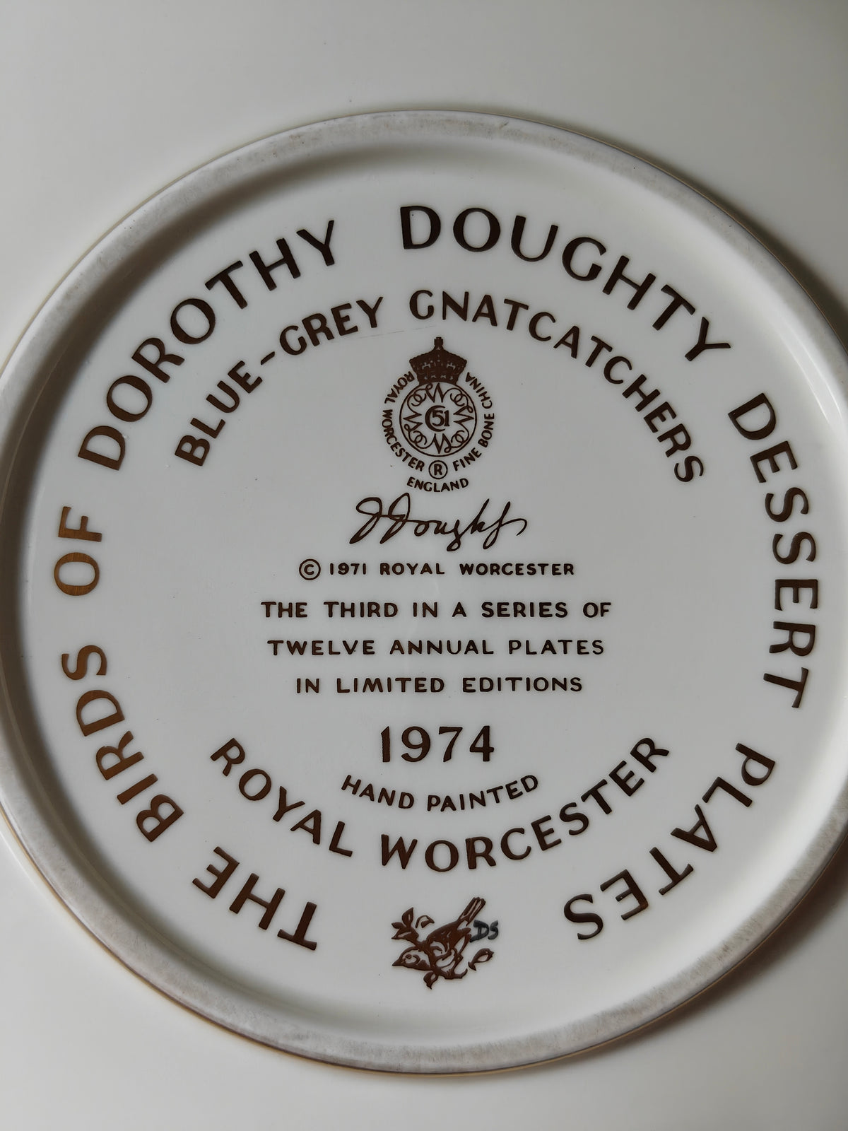 A close-up of the back of a Royal Worcester hand-painted ceramic plate, featuring brown printed text and logo for 'The Birds of Dorothy Doughty Dessert Plates' and 'Blue-Grey Gnatcatchers 1974'.