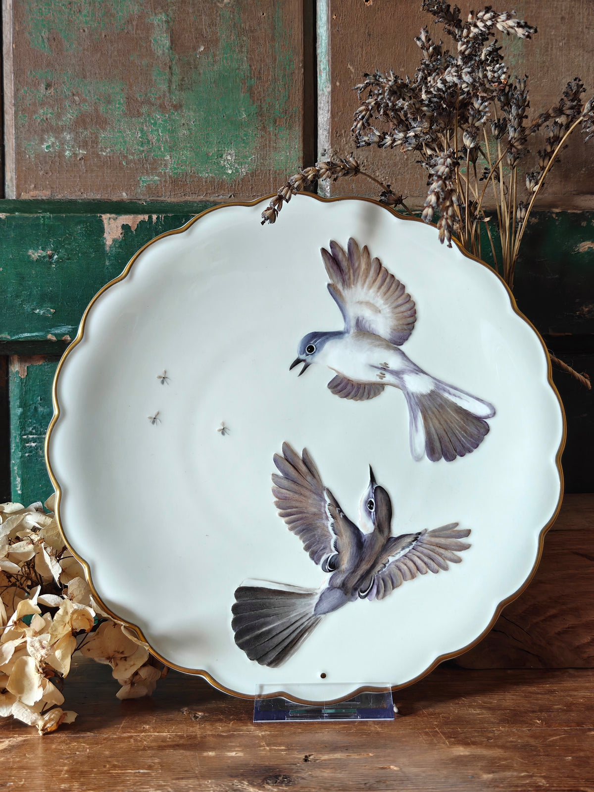 A scalloped white ceramic plate with a gold rim, featuring painted birds in flight.