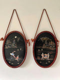 Two oval wall hangings with scenic illustrations on a plain background