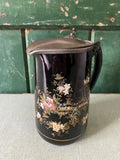 Decorative black jug with floral patterns and a metal lid 