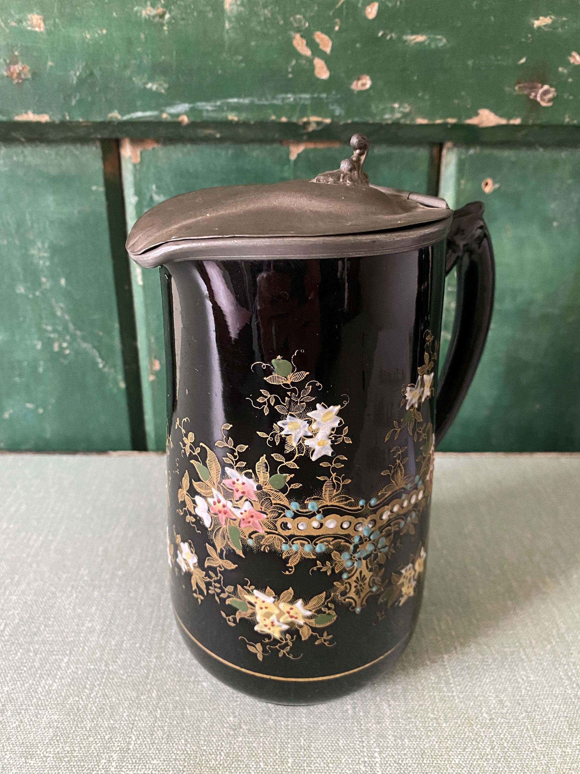 Decorative black jug with floral patterns and a metal lid 