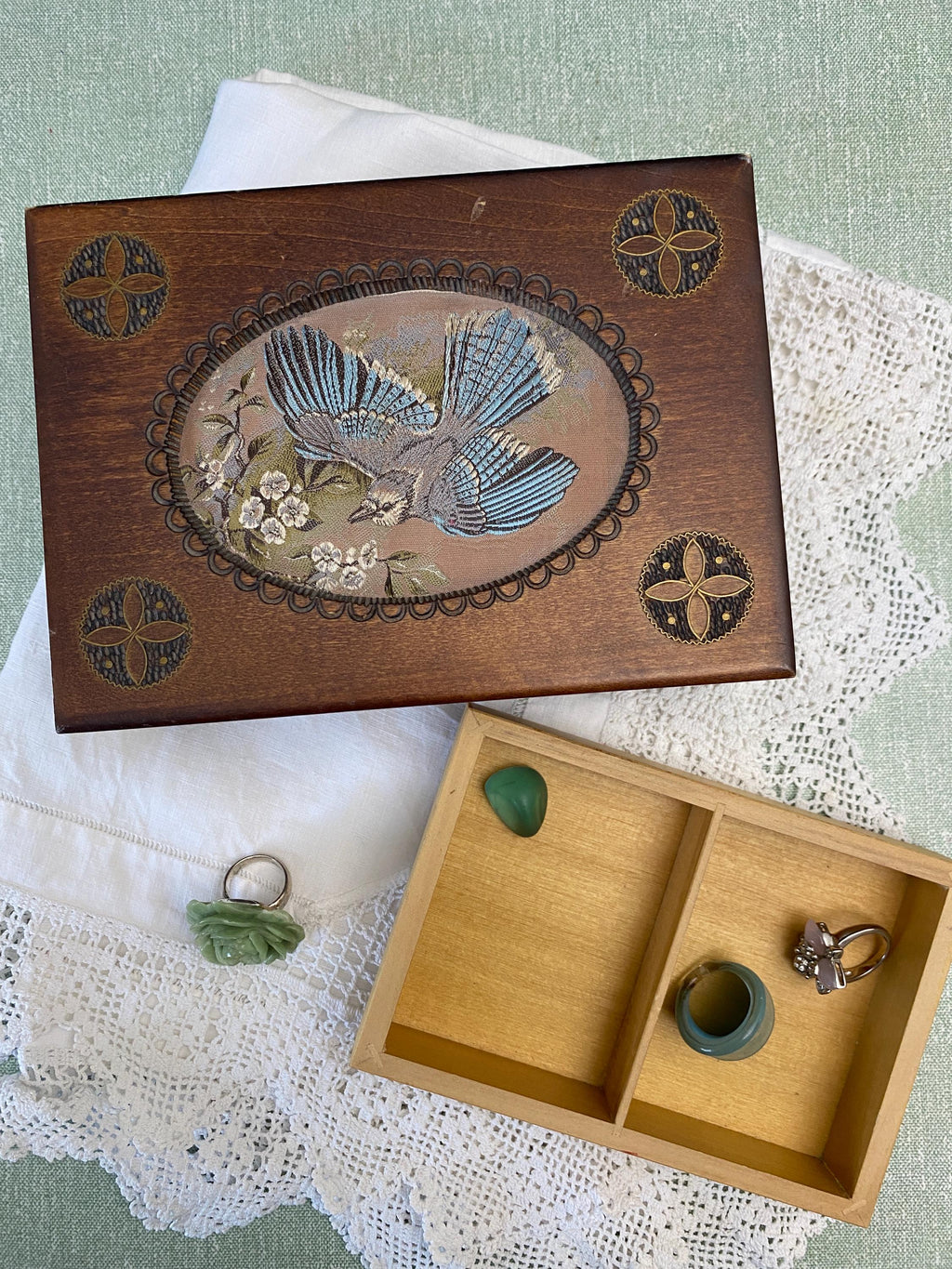 Wooden jewelry box with decorative lid featuring a bird design, open to reveal rings inside.