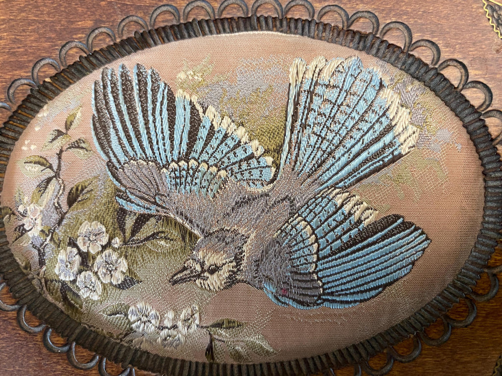 Embroidered design of a bird with floral elements on a wooden surface