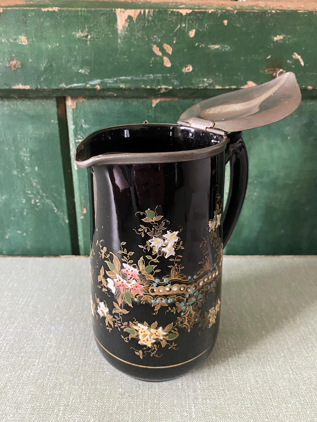 Decorative black jug with floral patterns and a metal hinged lid 