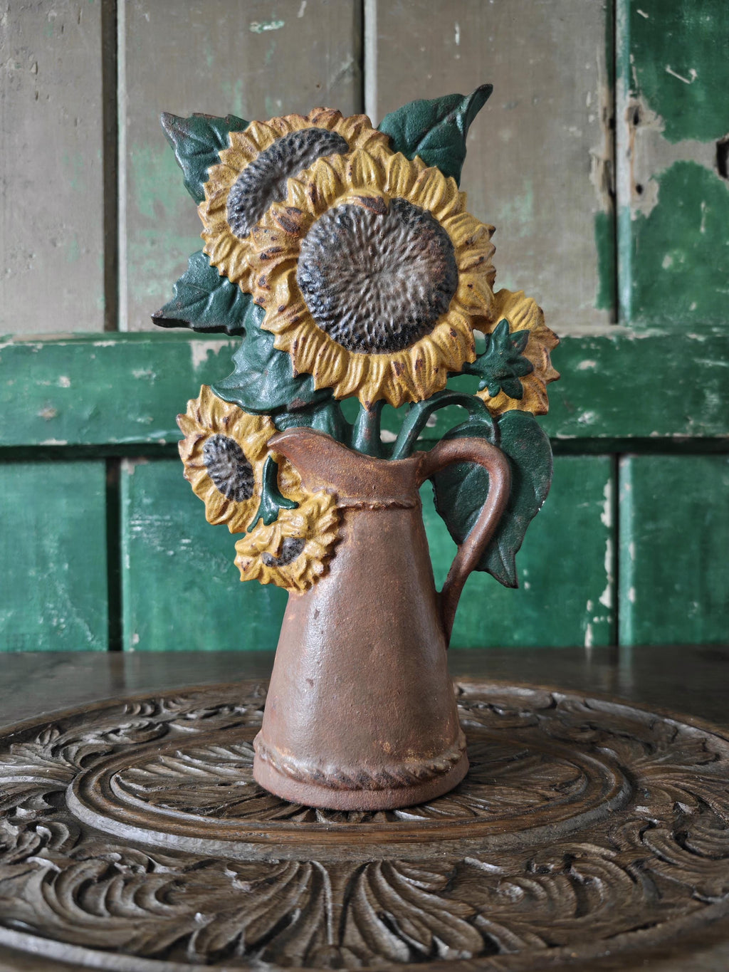 Decorative sunflower vase on a wooden surface with a green wooden panel background