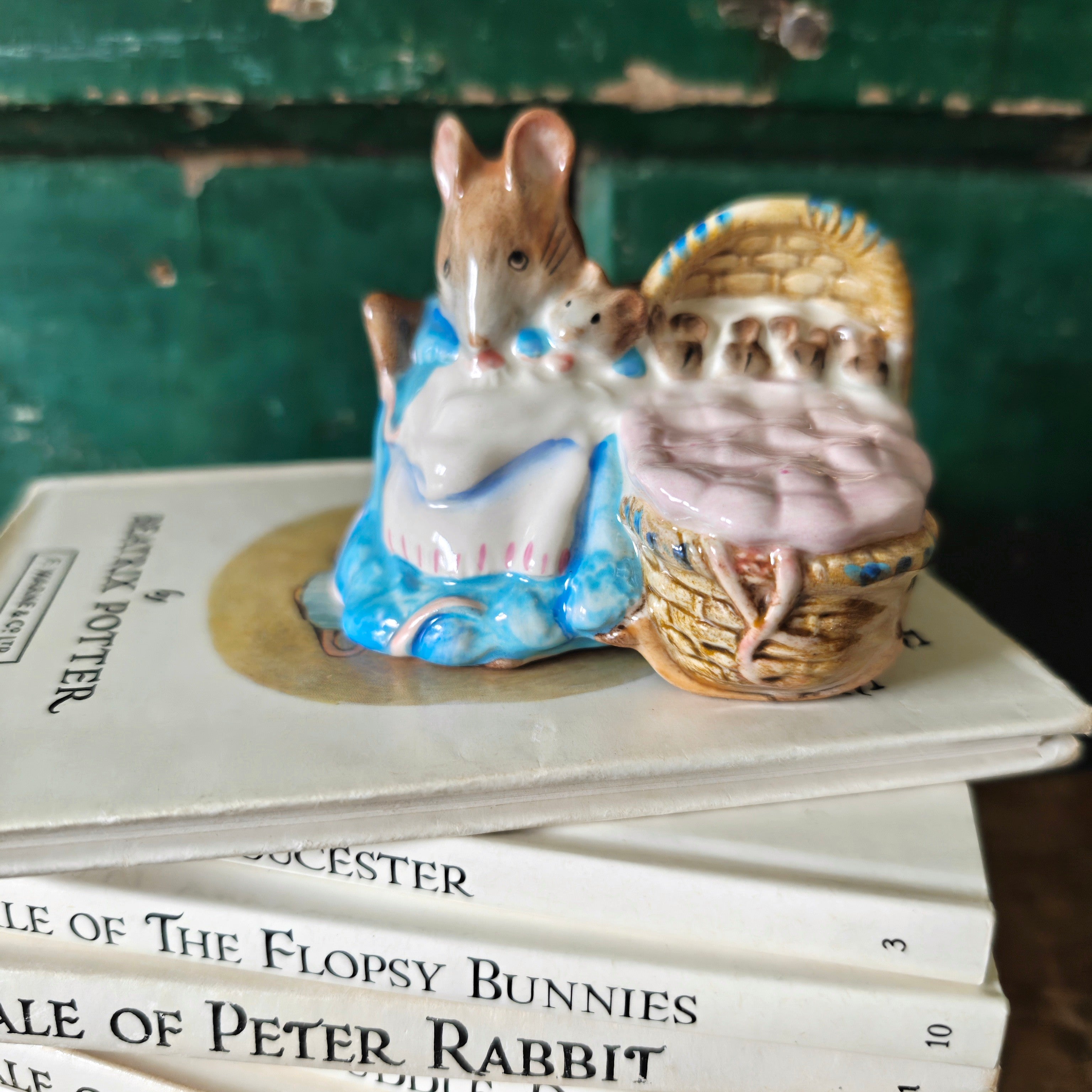 Ceramic figure of a mouse with a basket on top of 'The Tale of Peter Rabbit' books.