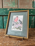 Framed artwork of two birds on a branch with flowers 