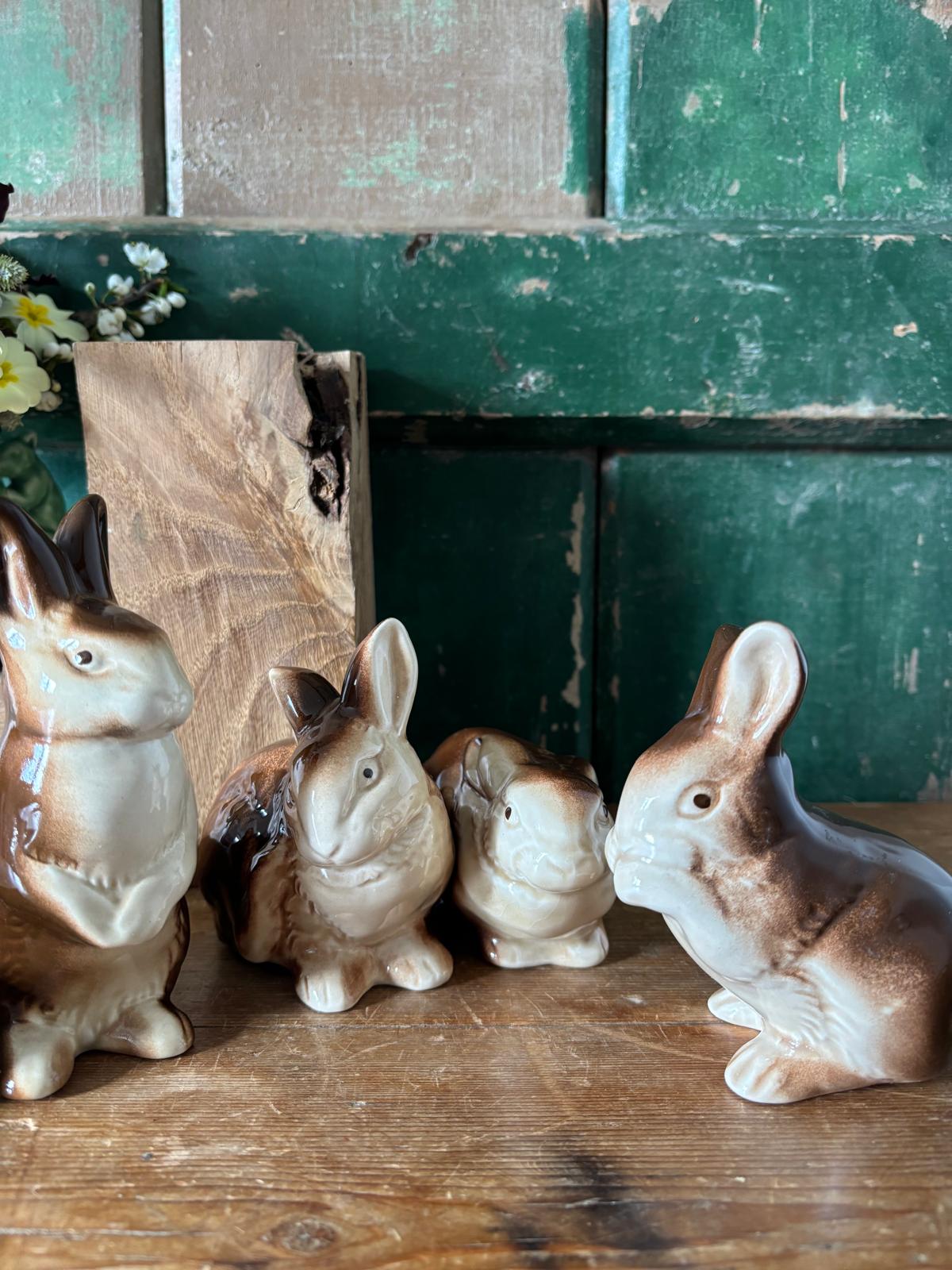 Four ceramic rabbit figurines on a wooden surface with a rustic green background.