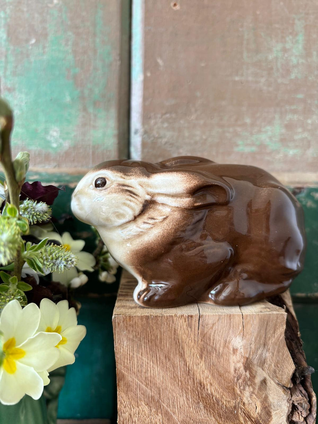 Brown ceramic rabbit figurine squatting with flowers in the background